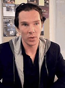 a man with a peachy head poster on the wall behind him looks at the camera