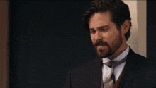 a man with a beard wearing a suit and tie stands in front of a door