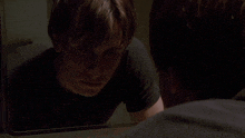 a man in a black shirt is looking at himself in the mirror