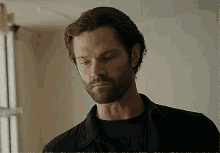 a man with a beard and a black shirt is looking down