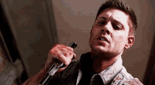 a man in a bloody shirt is holding a gun in his bloody hand .