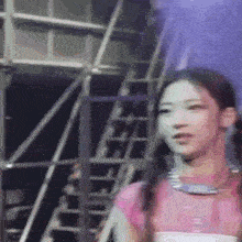 a girl in a pink shirt is standing in front of a staircase and looking at the camera .