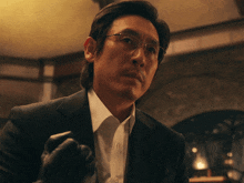 a man wearing glasses and a suit holds a glove in his hand