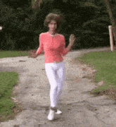a woman in a red shirt and white pants is walking down a sidewalk .