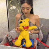 a woman is sitting on a couch holding a yellow teddy bear in a box .