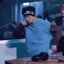 a man in a blue sweater is singing into a microphone while wearing a beanie .