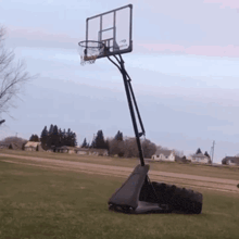a basketball hoop in a grassy field with a few houses in the background