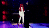 a woman with red hair is standing in a dark room with a man in a mask behind her .