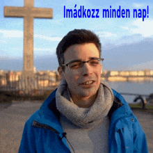 a man in a blue jacket is standing in front of a cross with the words imadkozz minden nap written above him