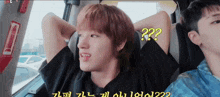 a man with red hair is sitting in a car with his head resting on his arm and a question mark on his face .