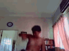 a shirtless man is dancing in a living room with a clock on the wall .