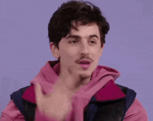a man in a pink jacket is pointing his finger at his face and says to the naked eye