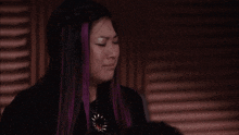 a woman with purple hair is crying while wearing a black shirt and a necklace .