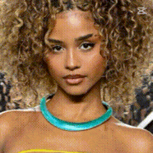 a close up of a woman 's face with curly hair wearing a blue necklace .