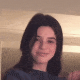a young girl with long dark hair is smiling and looking at the camera in a room .