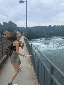 a woman is standing on a bridge over a river with her hair blowing in the wind