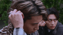 a man with a ring on his finger adjusts his hair while two other men look on