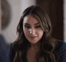 a woman wearing a blue jacket and a necklace looks at the camera