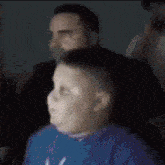 a boy in a blue shirt is sitting in front of a man .