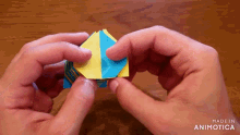 a person is holding a yellow and blue origami cube with the words made in animotica on the bottom