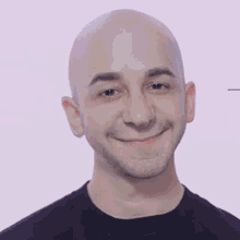 a bald man with a beard is smiling and wearing a black shirt