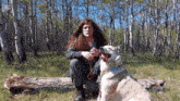 a man with long hair is sitting on a log with a dog .