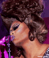 a drag queen is blowing a kiss into a microphone while wearing a leopard print top