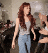 a woman with long red hair wearing a grey tank top and blue jeans
