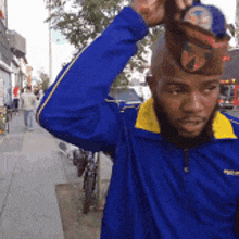 a man wearing a blue jacket and a yellow collar is holding a hat on his head