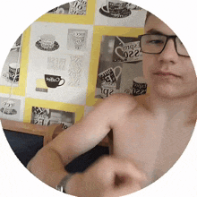 a shirtless man wearing glasses stands in front of a wall with coffee cups and saucers