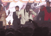 a man in a white suit is dancing in front of a crowd with the word oct on the screen
