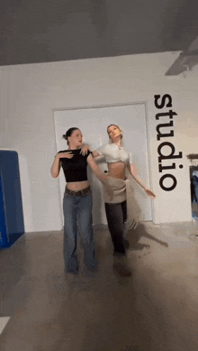 two women are dancing in a room with the word studio on the wall .