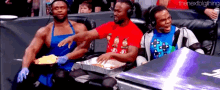three men wearing aprons and headphones are sitting in a stadium eating food from a tray .