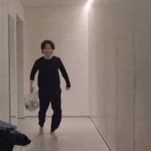a man in a black shirt is walking down a hallway holding a plastic bag .
