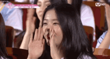 a woman is sitting in a stadium with her hands on her face and a mnet logo behind her