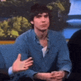 a man in a blue shirt is sitting on a couch and talking .