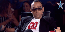 a man wearing sunglasses and a skull shirt is sitting in a chair