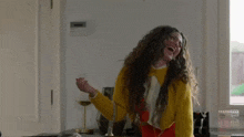 a woman with curly hair is wearing a yellow sweater and laughing .