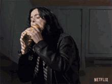 a woman in a black leather jacket is eating a hamburger with netflix written on the bottom