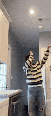 a man in a yellow and black striped sweater is hanging a light fixture from the ceiling