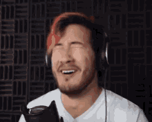 a man with red hair is wearing headphones and laughing while holding a microphone .