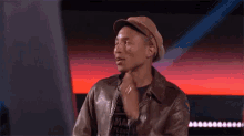 a man wearing a hat and a leather jacket is making a funny face on a stage .