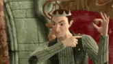 a cartoon character is sitting in a chair wearing a crown and pointing at the camera .