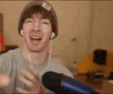 a man wearing headphones and a beanie is standing in front of a microphone and laughing .
