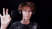 a young man wearing headphones and glasses is making a funny face and pointing at his finger .