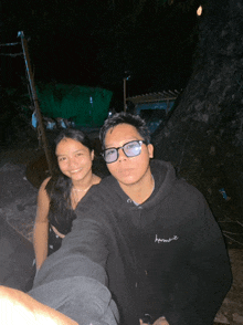 a man and a woman are posing for a picture and the man is wearing a black hoodie with the word harmony on it