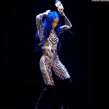 a woman with blue hair is holding a microphone in her hand while wearing a silver and gold outfit .
