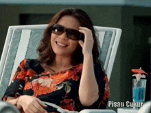 a woman wearing sunglasses is smiling while sitting in a chair with pisau cukur written below her