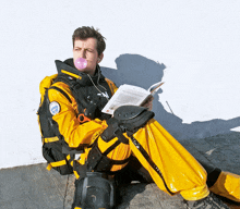 a man blowing a bubble while reading a book and wearing a jacket that says rescue
