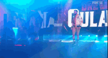 a man in a bomber jacket is walking on a stage in front of a sign that says drew gula .